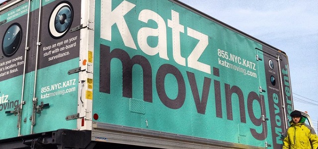 A teal blue Katz Moving truck with white and black font coloring with a worker in a yellow jacket.
