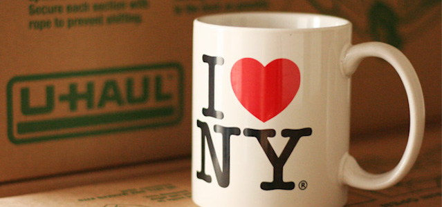 A white I Love New York coffee mug sitting on a table with a brown cardboard moving box in the background.